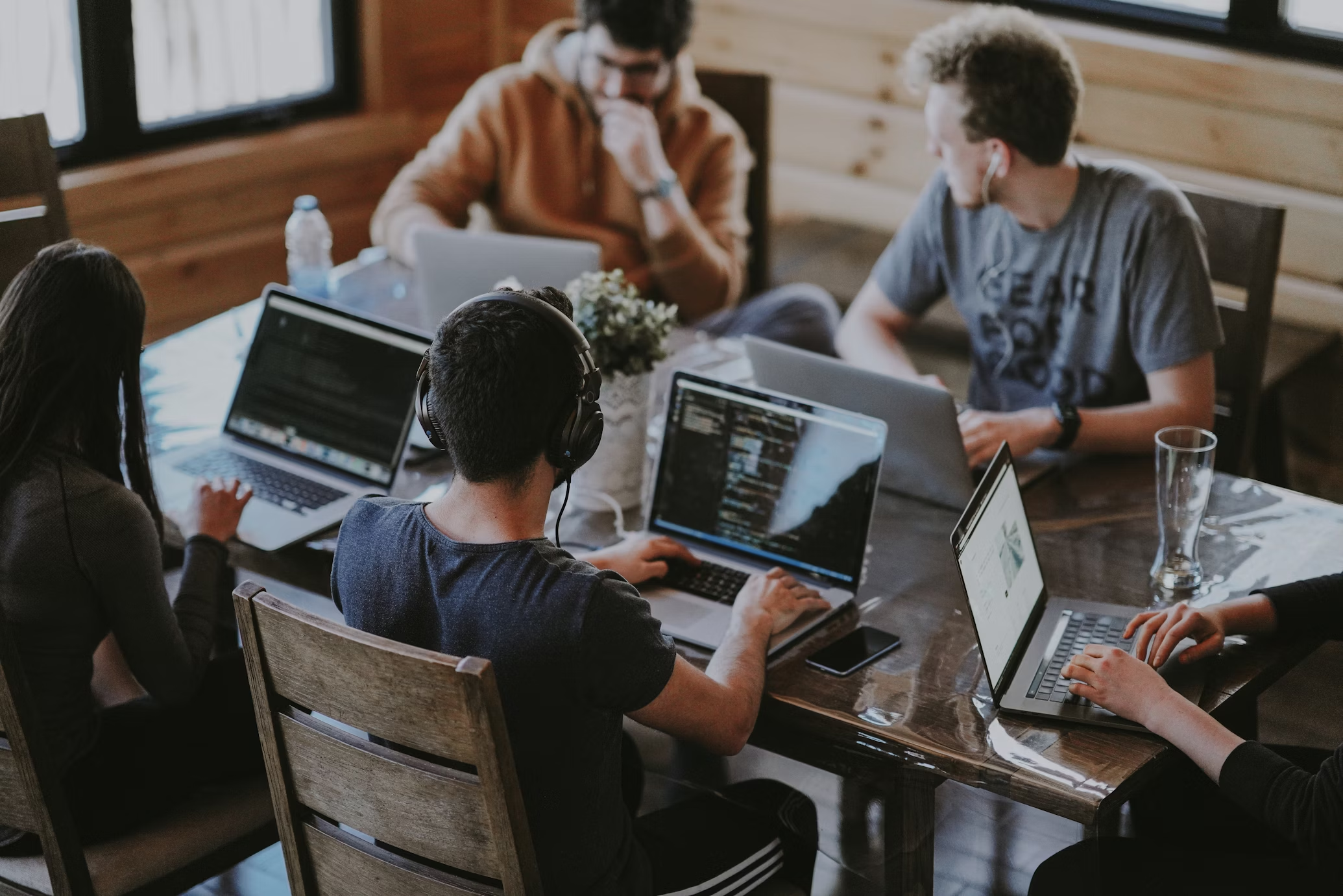 A group of people sit at a communal table and work on their laptops together.